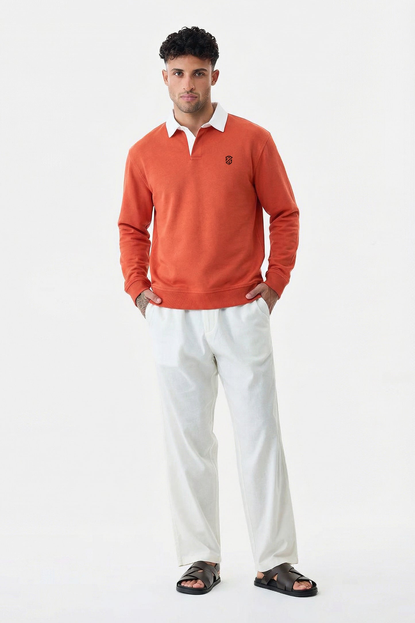 Man modeling orange pullover, white pants, and black sandals on white background