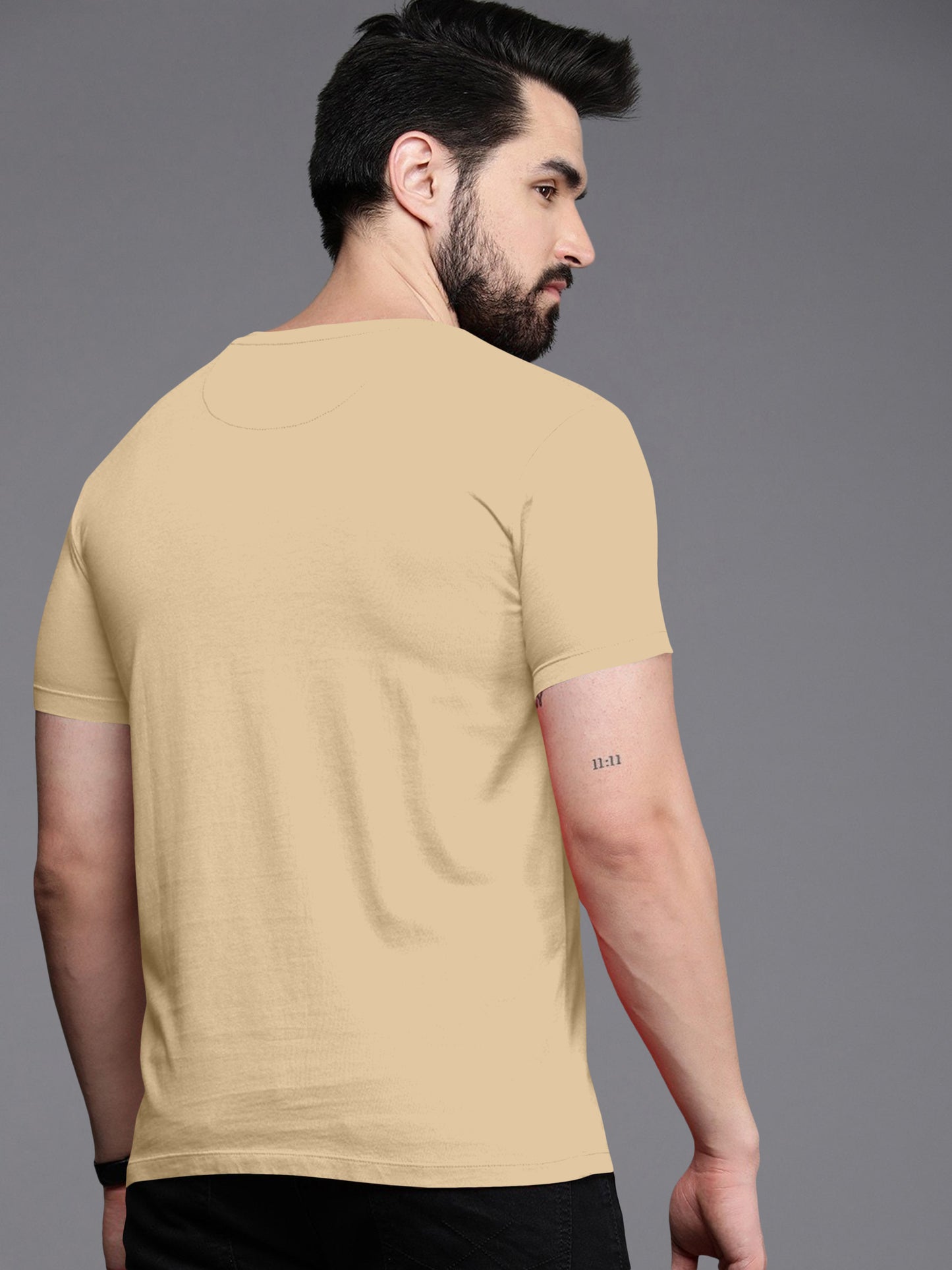 Man wearing beige short sleeve t-shirt, back view, tattoo on arm, neutral background