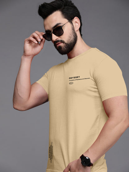 Man wearing beige graphic t-shirt with 'Odyssey' text, sunglasses, and wristwatch