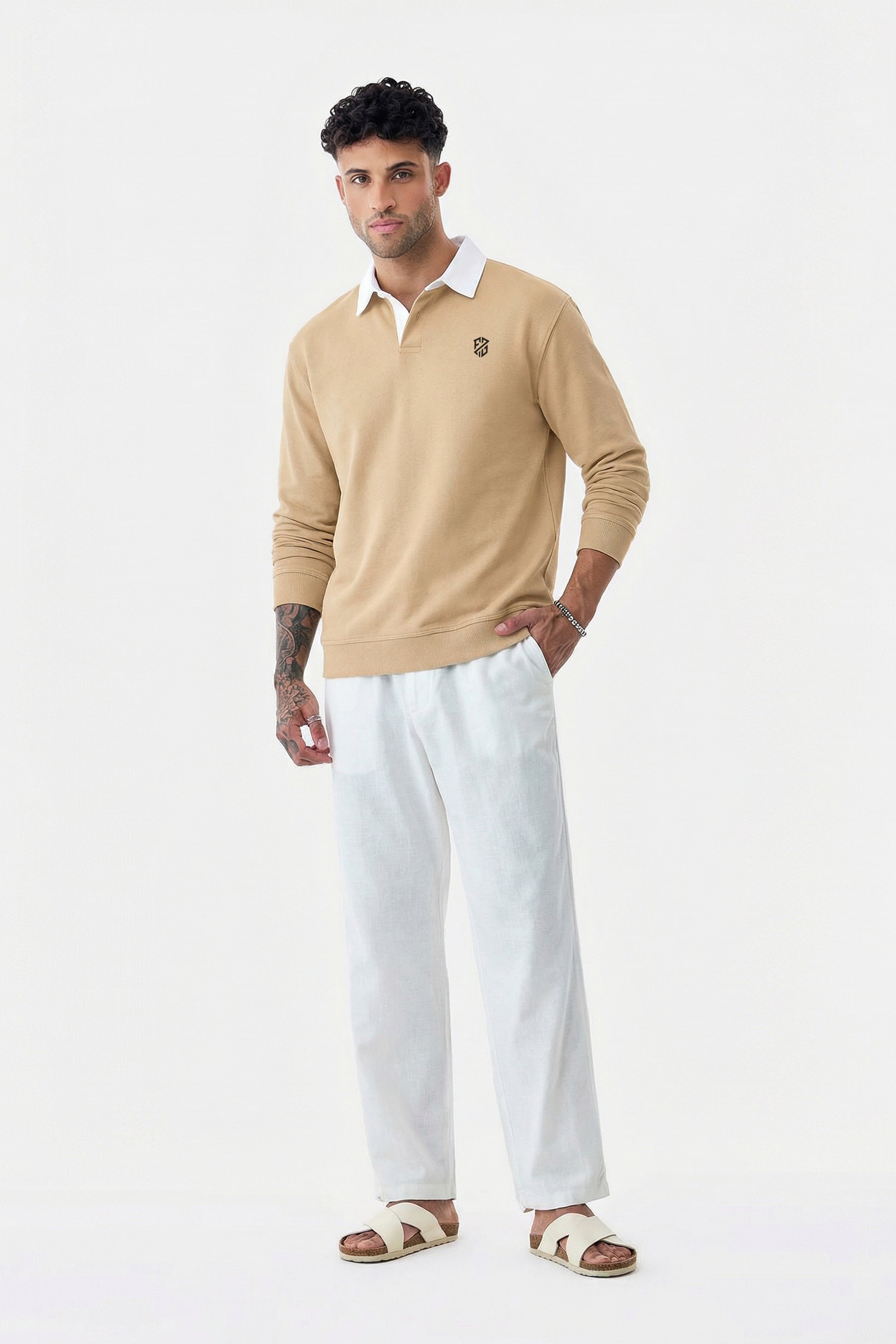 Man in beige long-sleeve polo, white pants, and sandals posing on white background