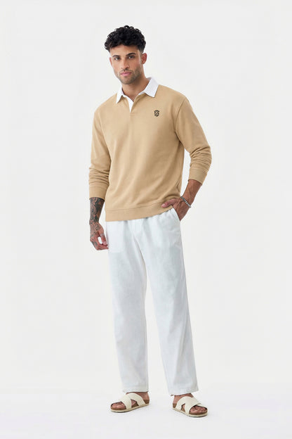 Man in beige long-sleeve polo, white pants, and sandals posing on white background