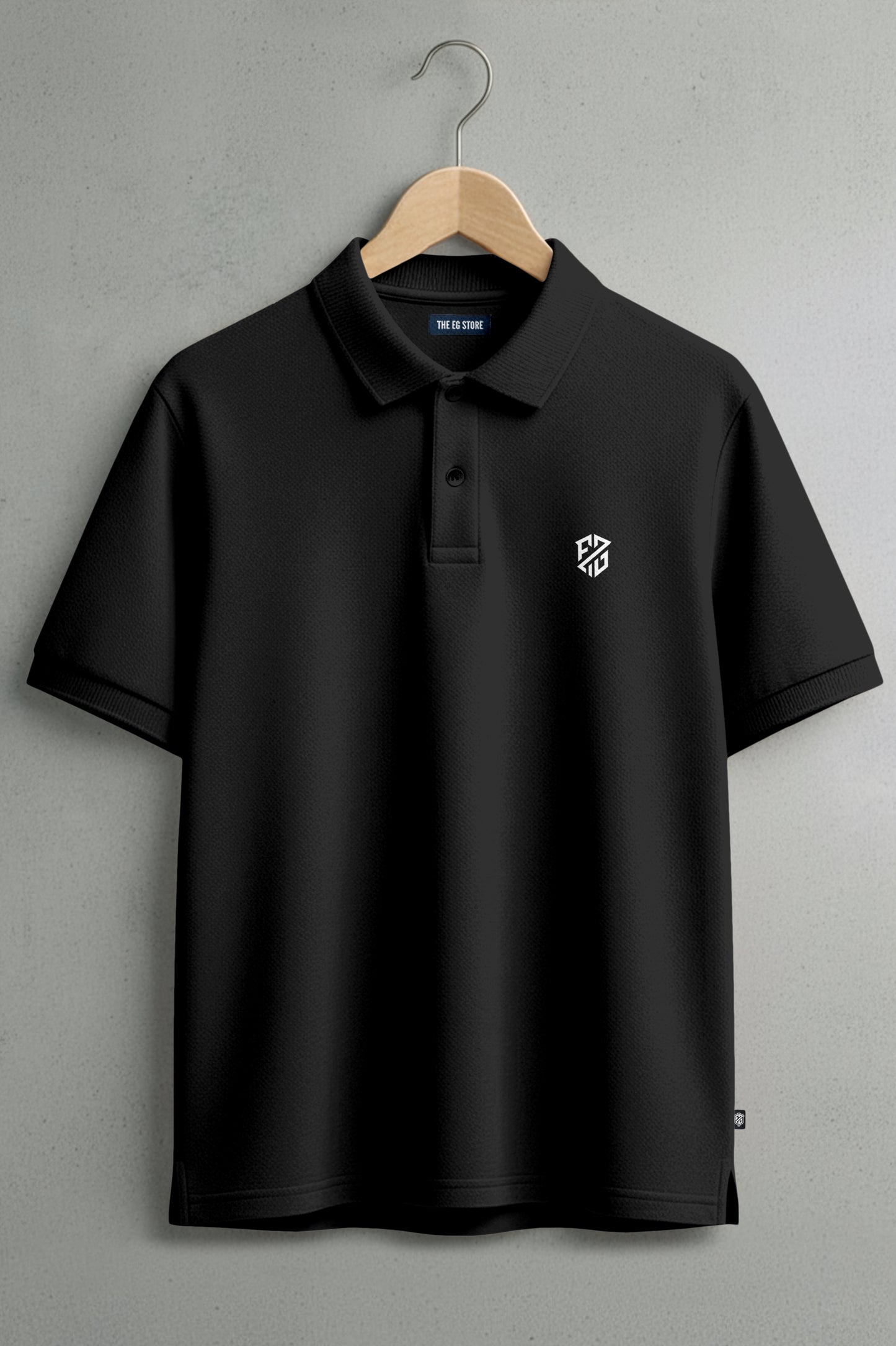 Black polo shirt with white embroidered logo on chest, hanging on wooden hanger
