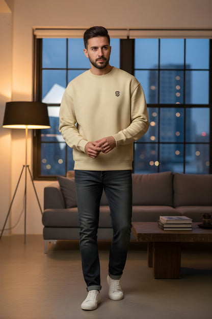 Man in beige crewneck sweatshirt, dark jeans, and white sneakers standing in modern living room