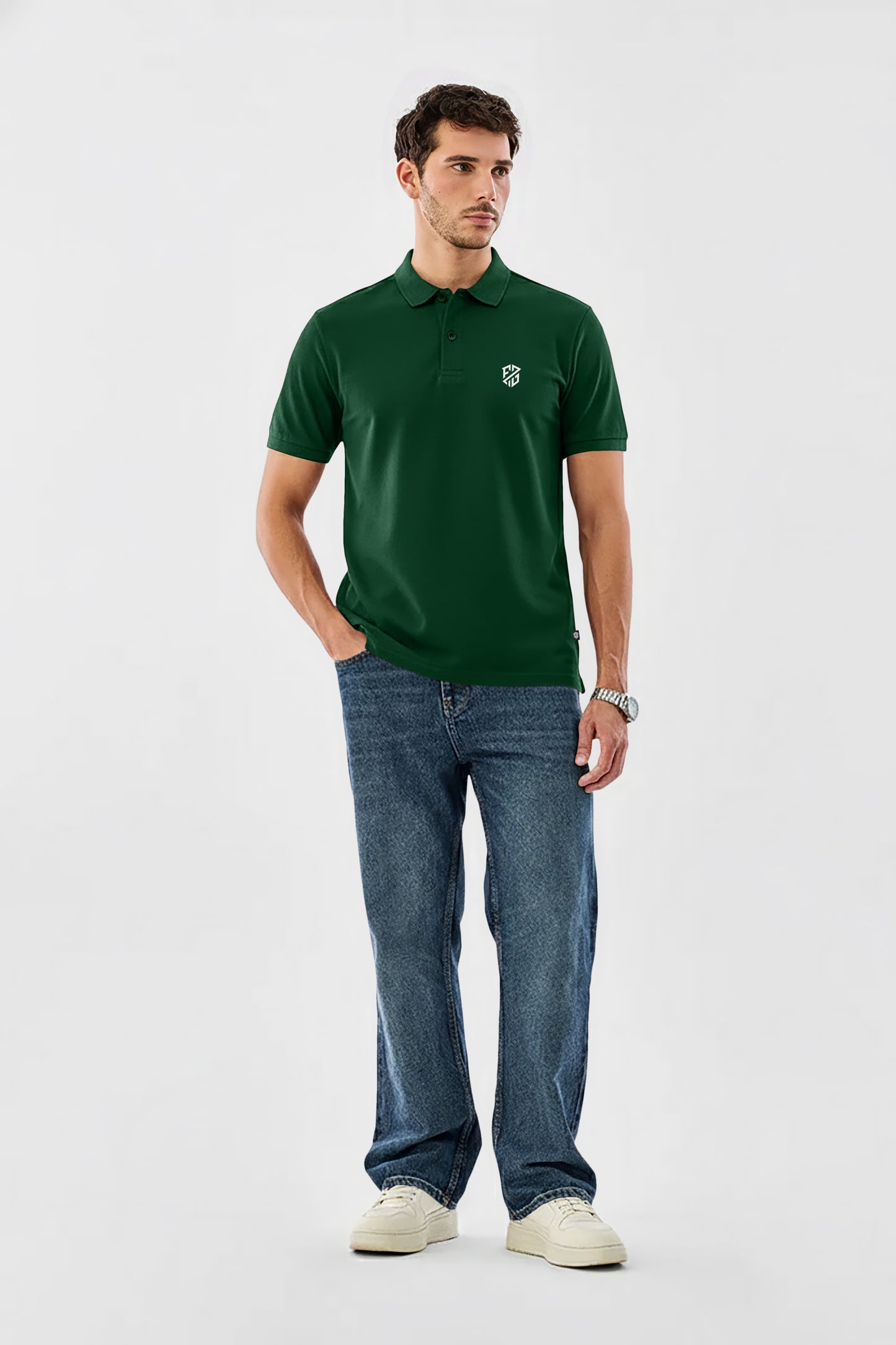 Man in green polo shirt with white logo, blue jeans, and white sneakers on plain background