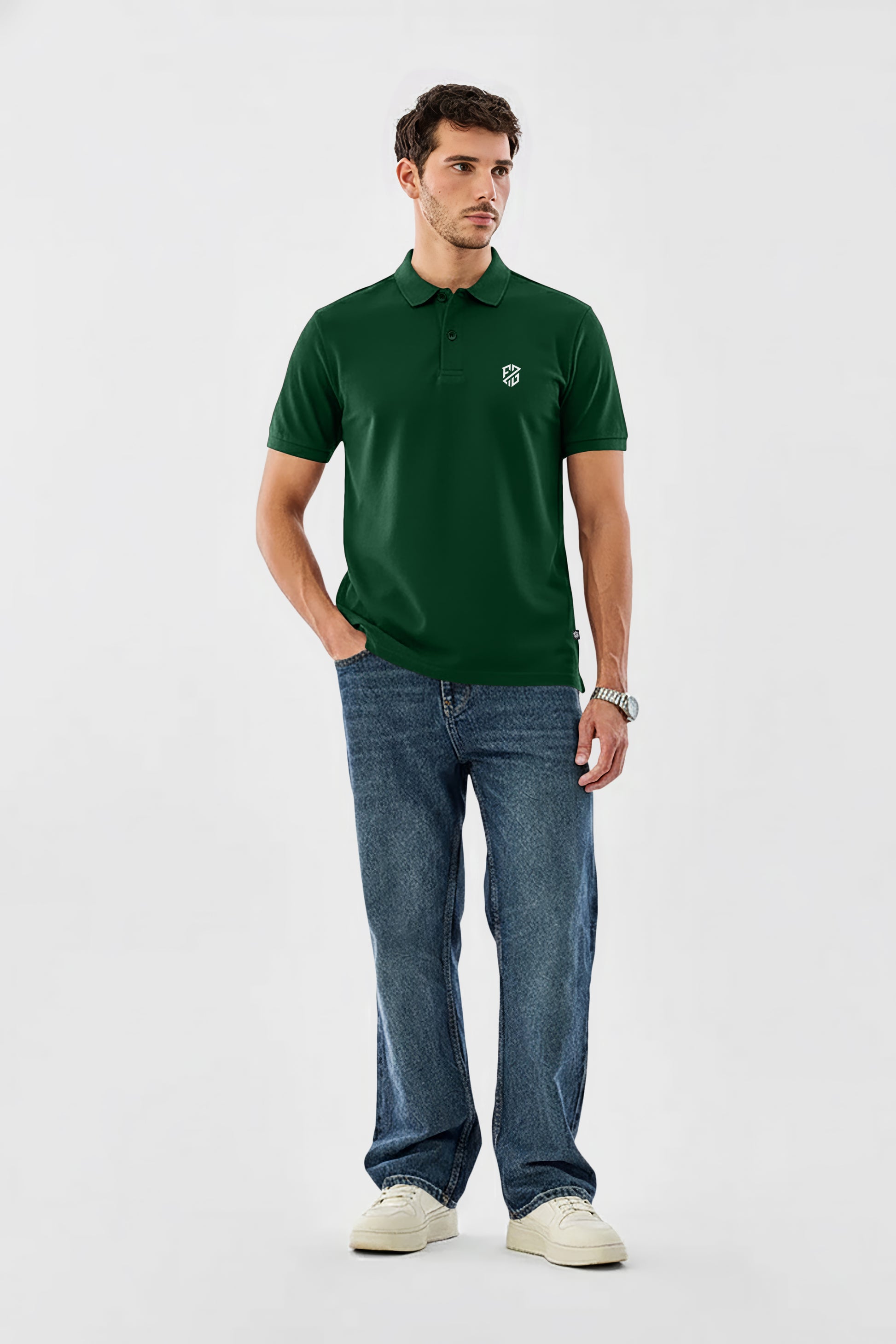 Man in green polo shirt with white logo, blue jeans, and white sneakers on plain background