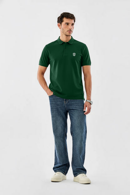 Man in green polo shirt with white logo, blue jeans, and white sneakers on plain background