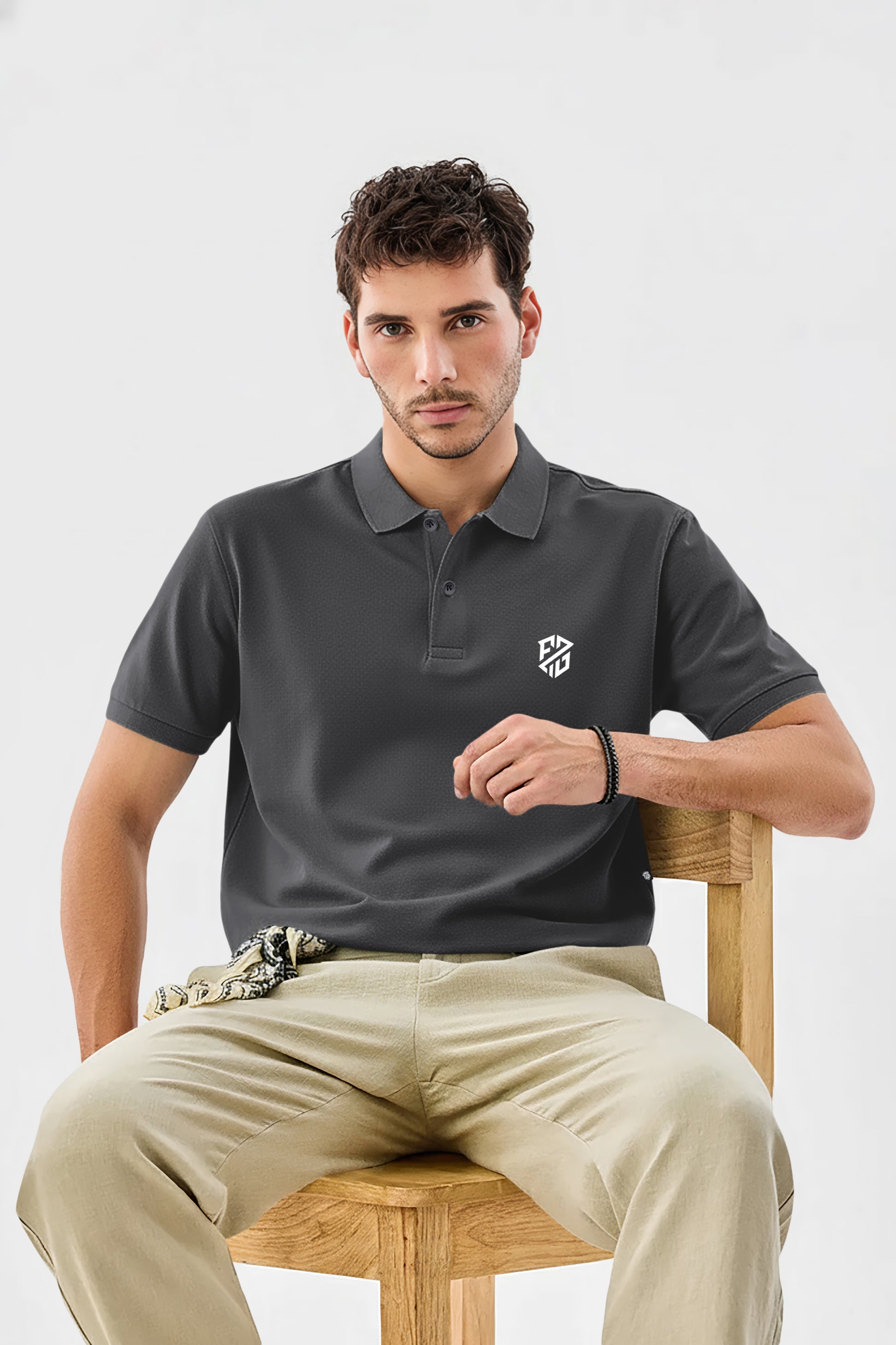 Man wearing dark gray short sleeve polo shirt with white logo, sitting on a wooden chair
