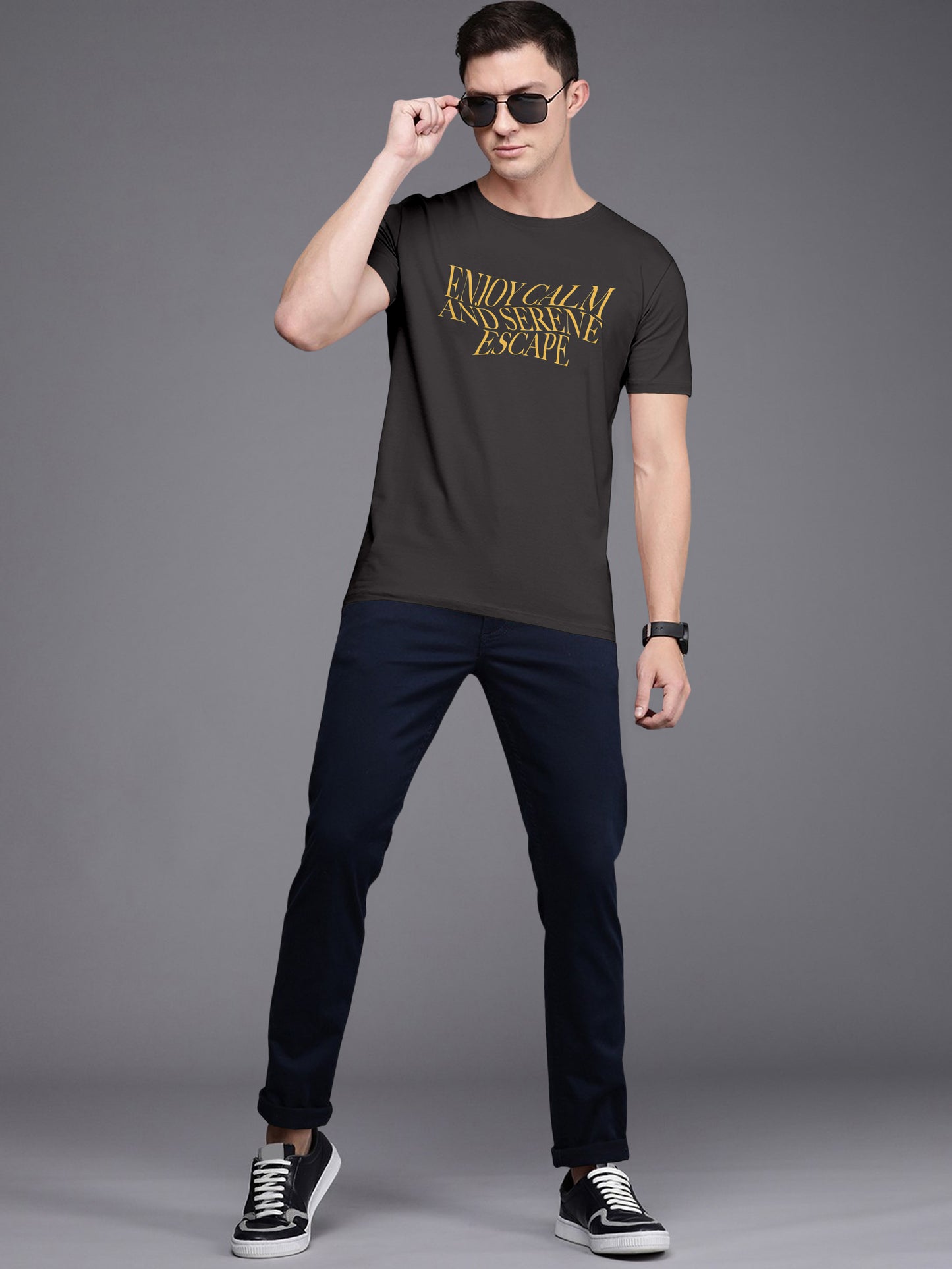 Man wearing black graphic t-shirt with yellow text, navy pants, sunglasses, and sneakers