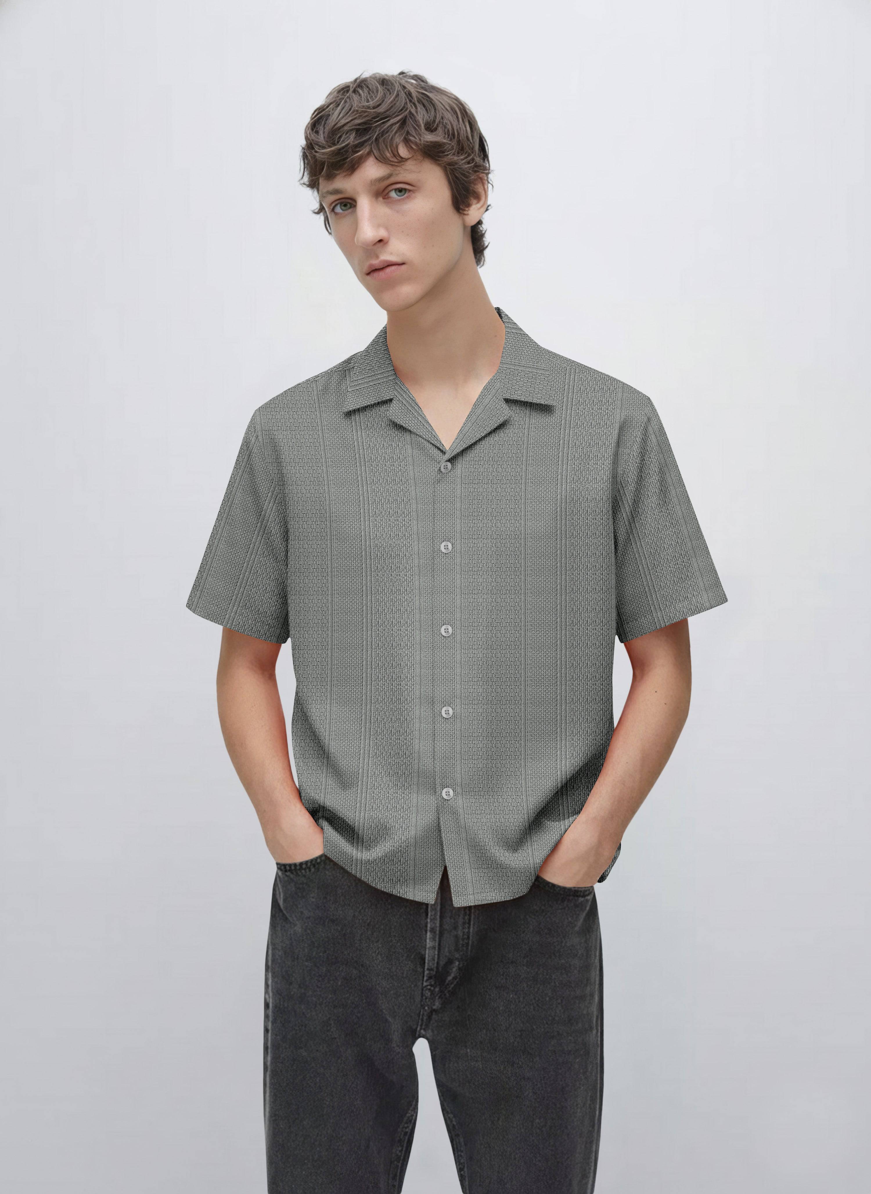 Man wearing textured short sleeve gray button-up shirt and black jeans, minimal background