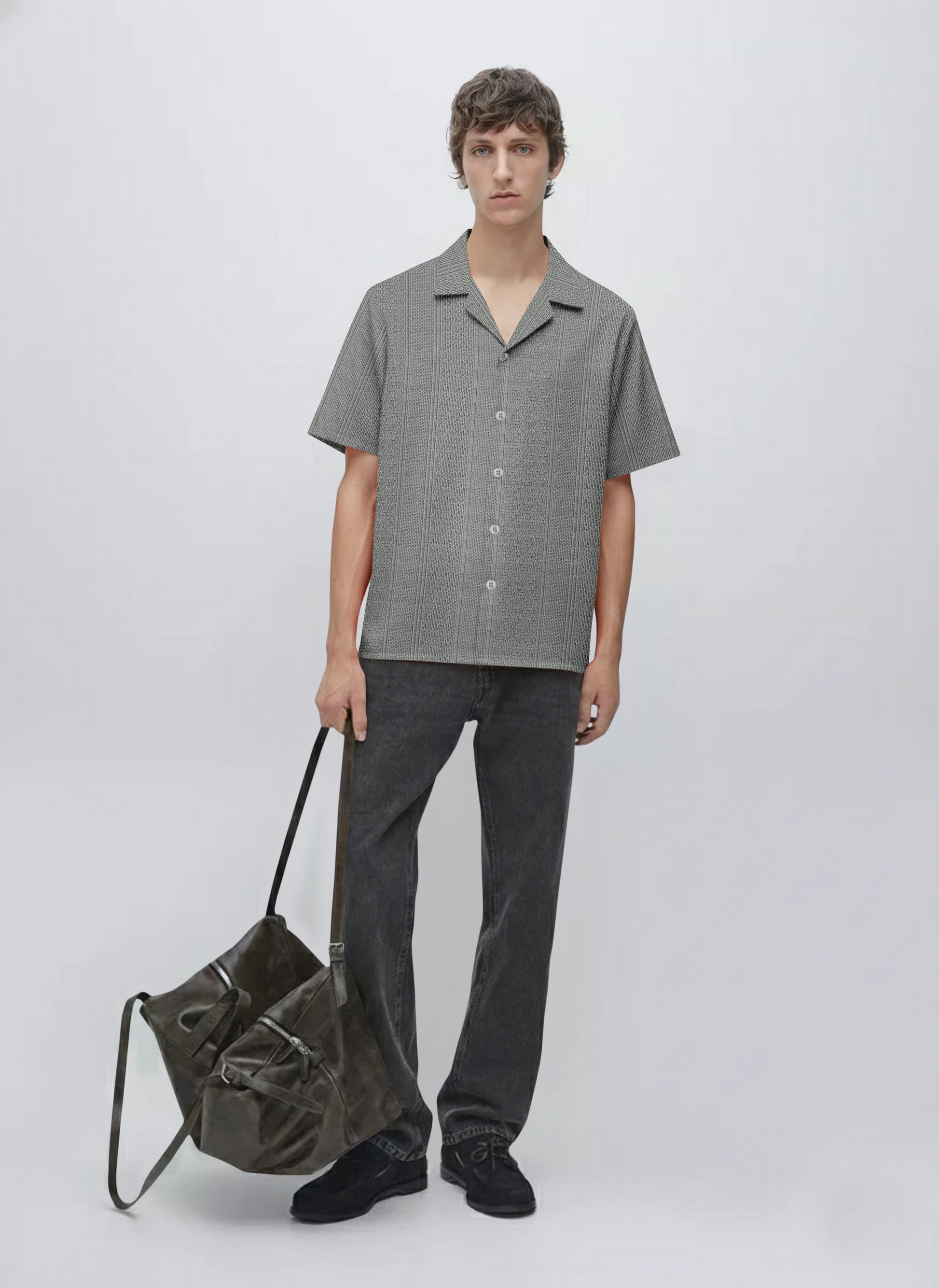 Man in short sleeve patterned shirt, black jeans, holding large dark shoulder bag