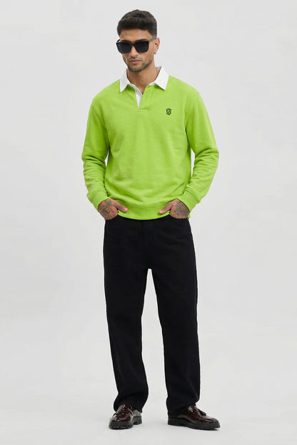 Man wearing lime green long-sleeve polo shirt, black pants, and sunglasses, standing indoors