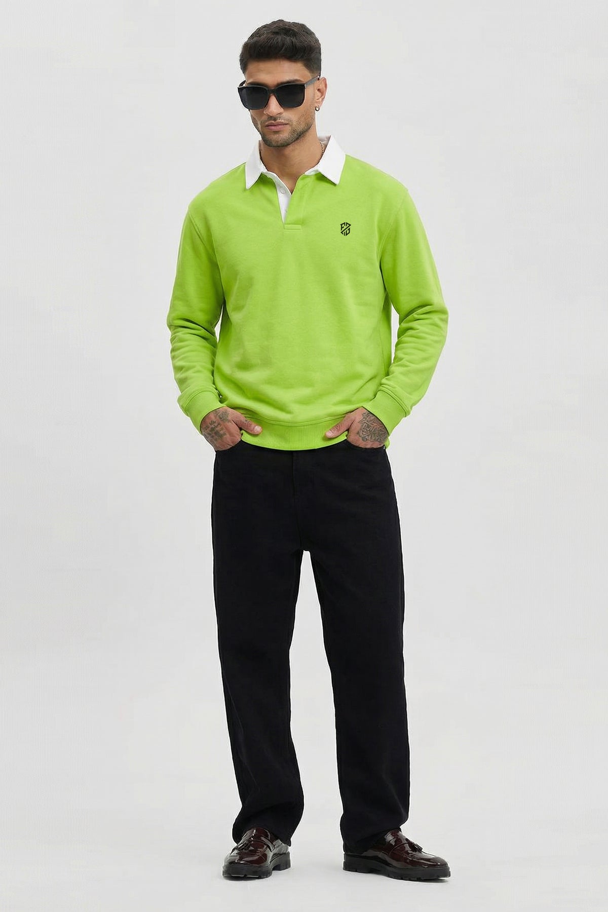 Man wearing lime green long-sleeve polo shirt, black pants, and sunglasses, standing indoors