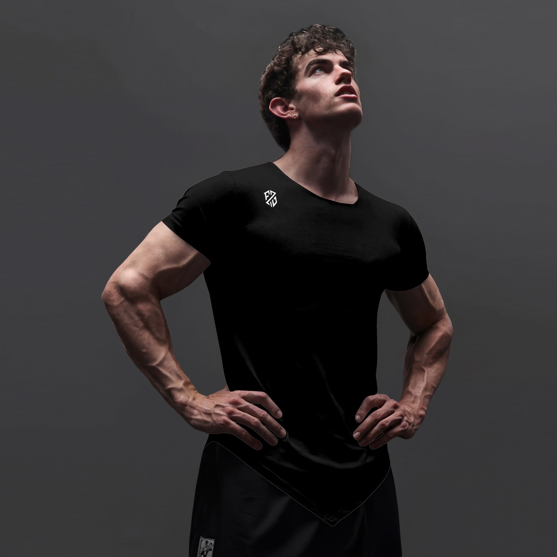 Athletic man wearing a fitted black workout t-shirt and shorts on a dark background