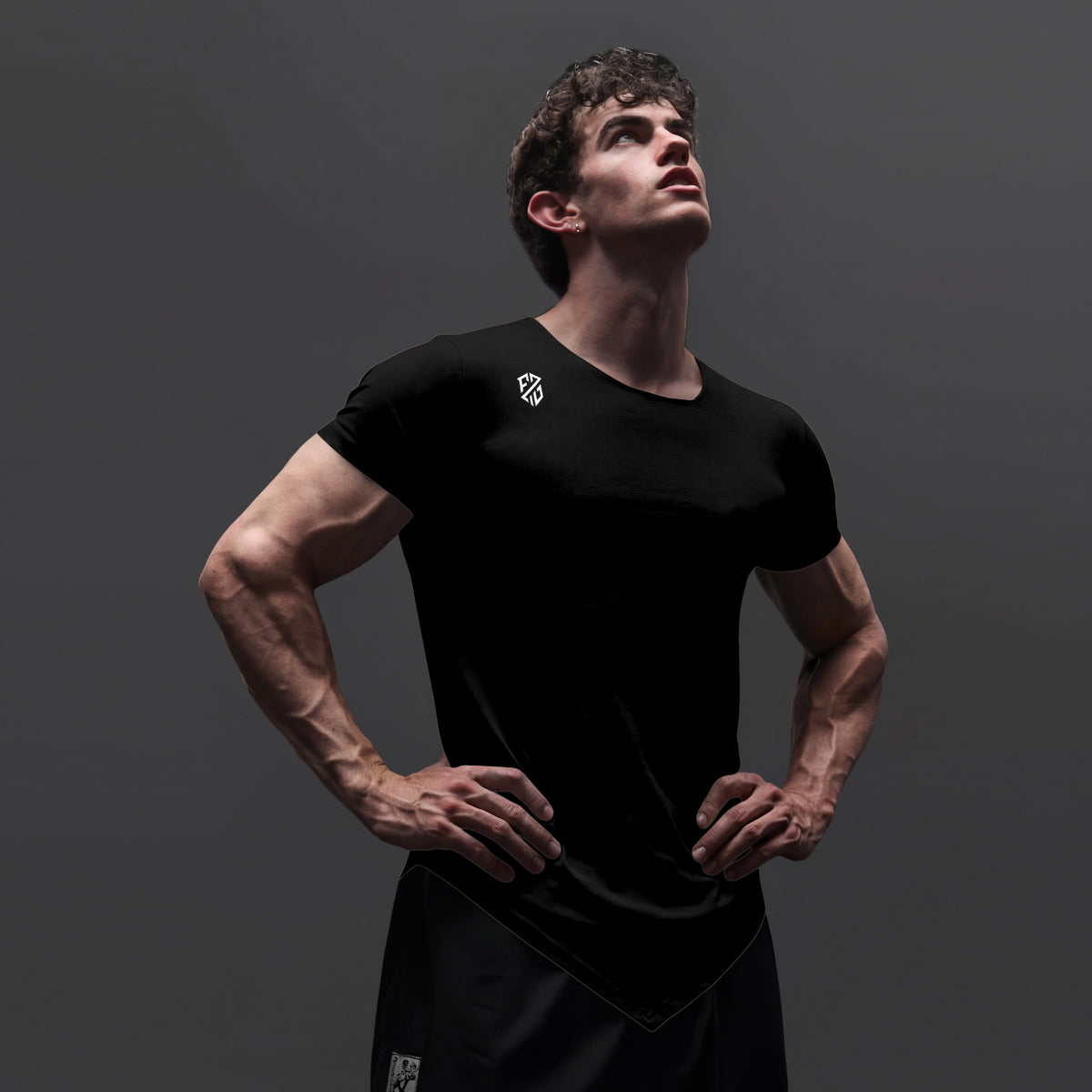Athletic man wearing a fitted black workout t-shirt and shorts on a dark background