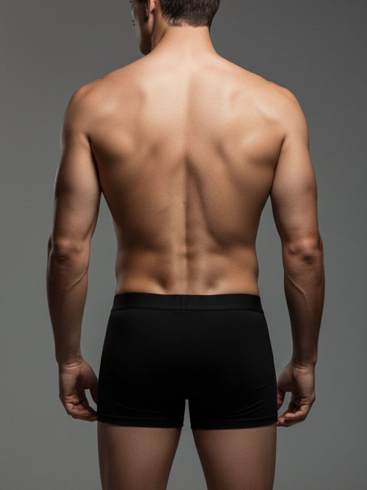 Back view of man wearing black fitted boxer briefs on plain background