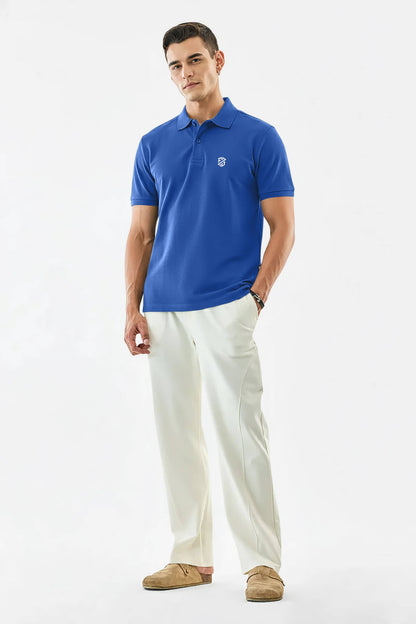 Man in blue polo shirt with emblem, white trousers, and tan loafers on white background