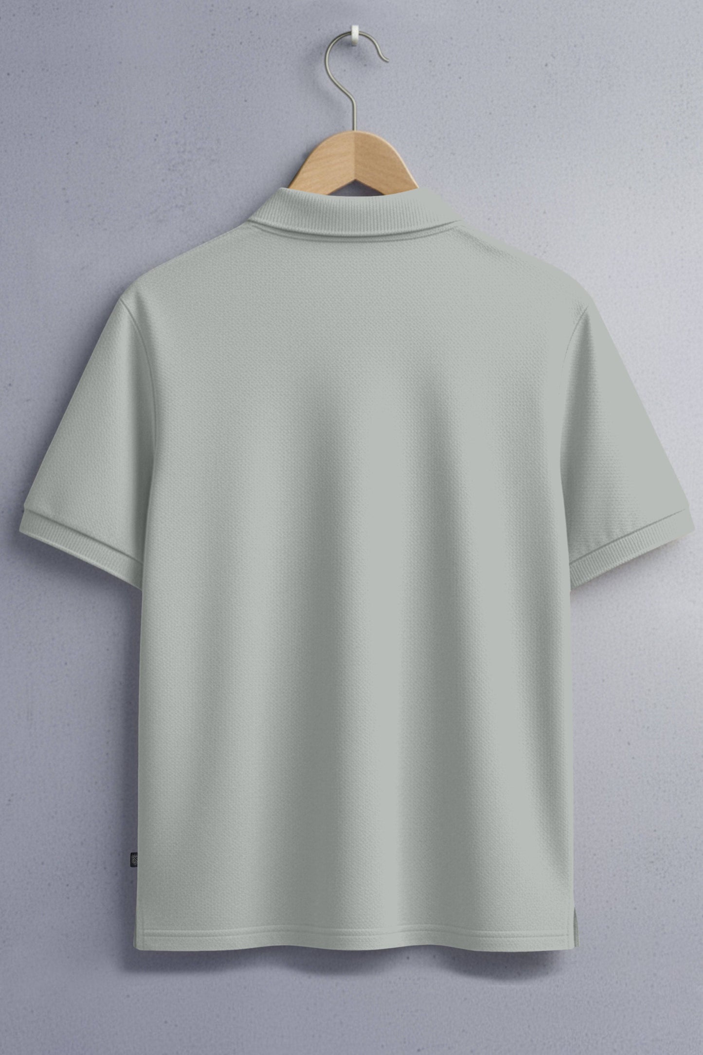 Light grey short-sleeve polo shirt on a hanger against a textured wall