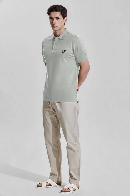 Man wearing light grey polo shirt, beige pants, and white sandals on neutral background
