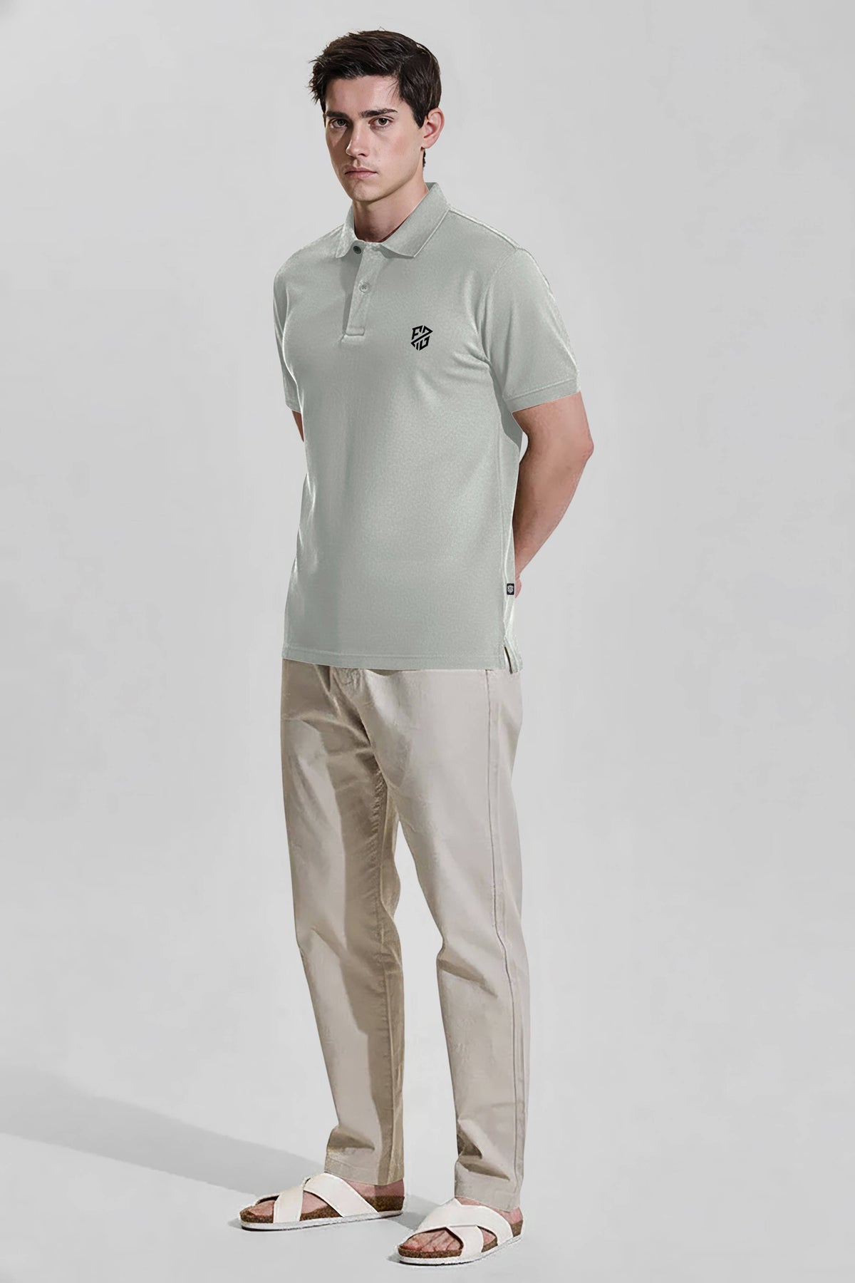 Man wearing light grey polo shirt, beige pants, and white sandals on neutral background
