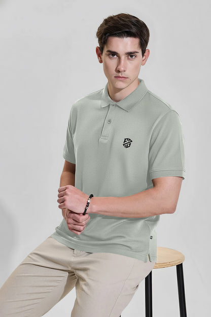 Man wearing light grey short sleeve polo shirt with logo and beige pants, seated on stool