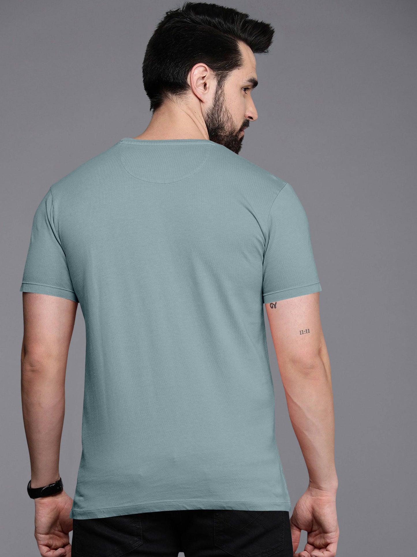 Man wearing light blue short sleeve t-shirt, back view, plain grey background