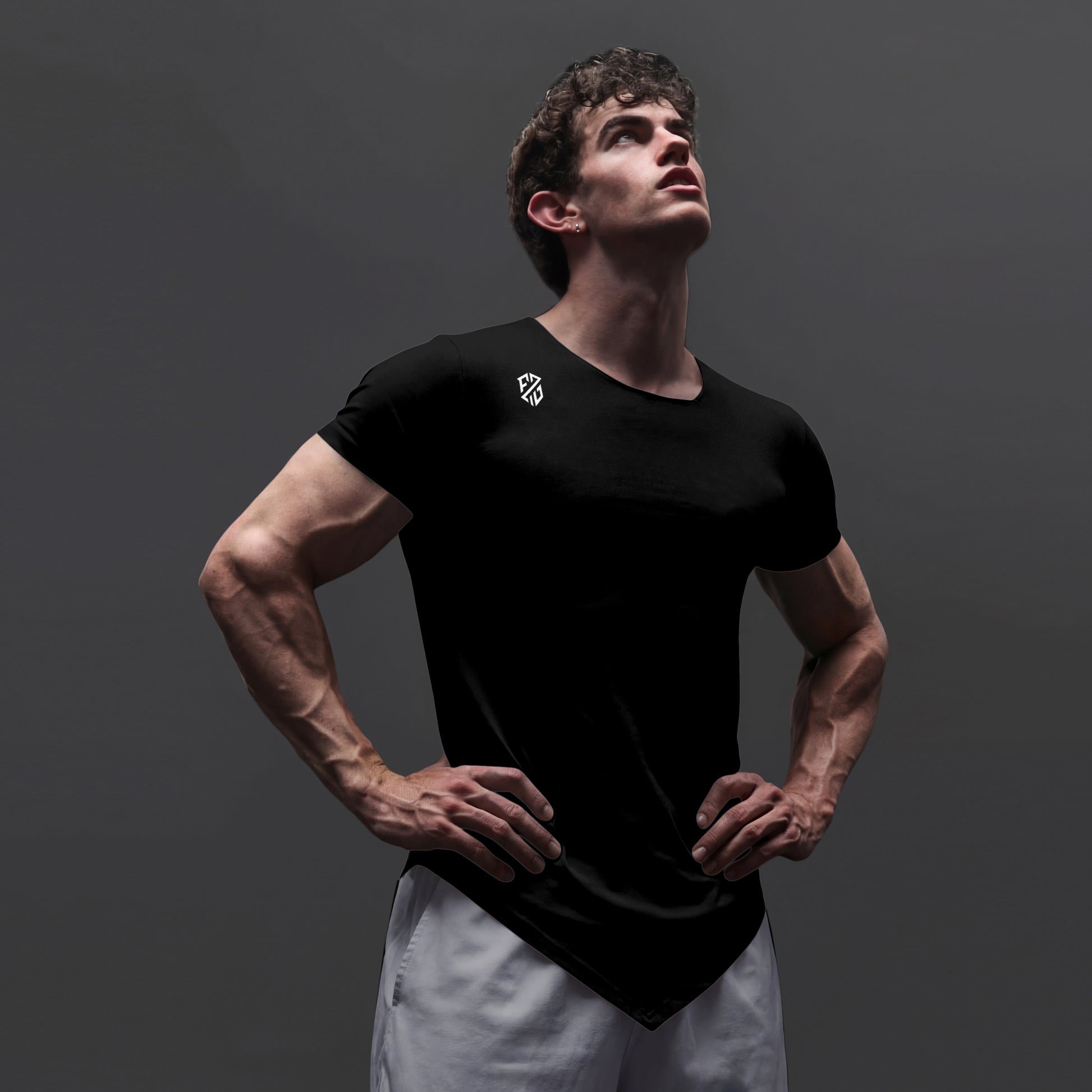 Athletic man in black fitted t-shirt with logo, hands on hips, standing against gray background