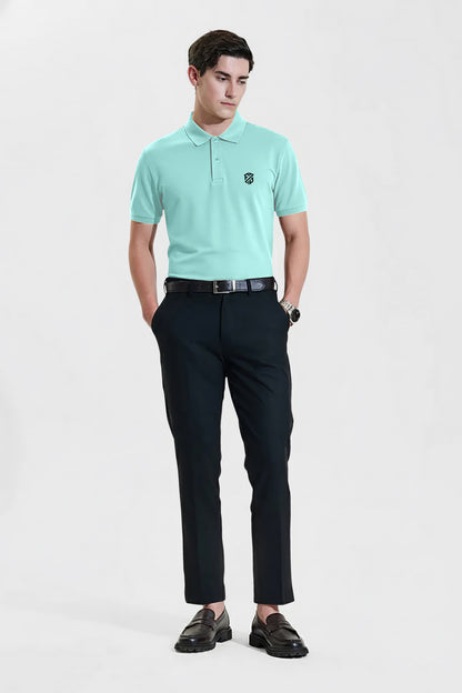 Man wearing mint green polo shirt with logo and black dress pants, standing on white background.