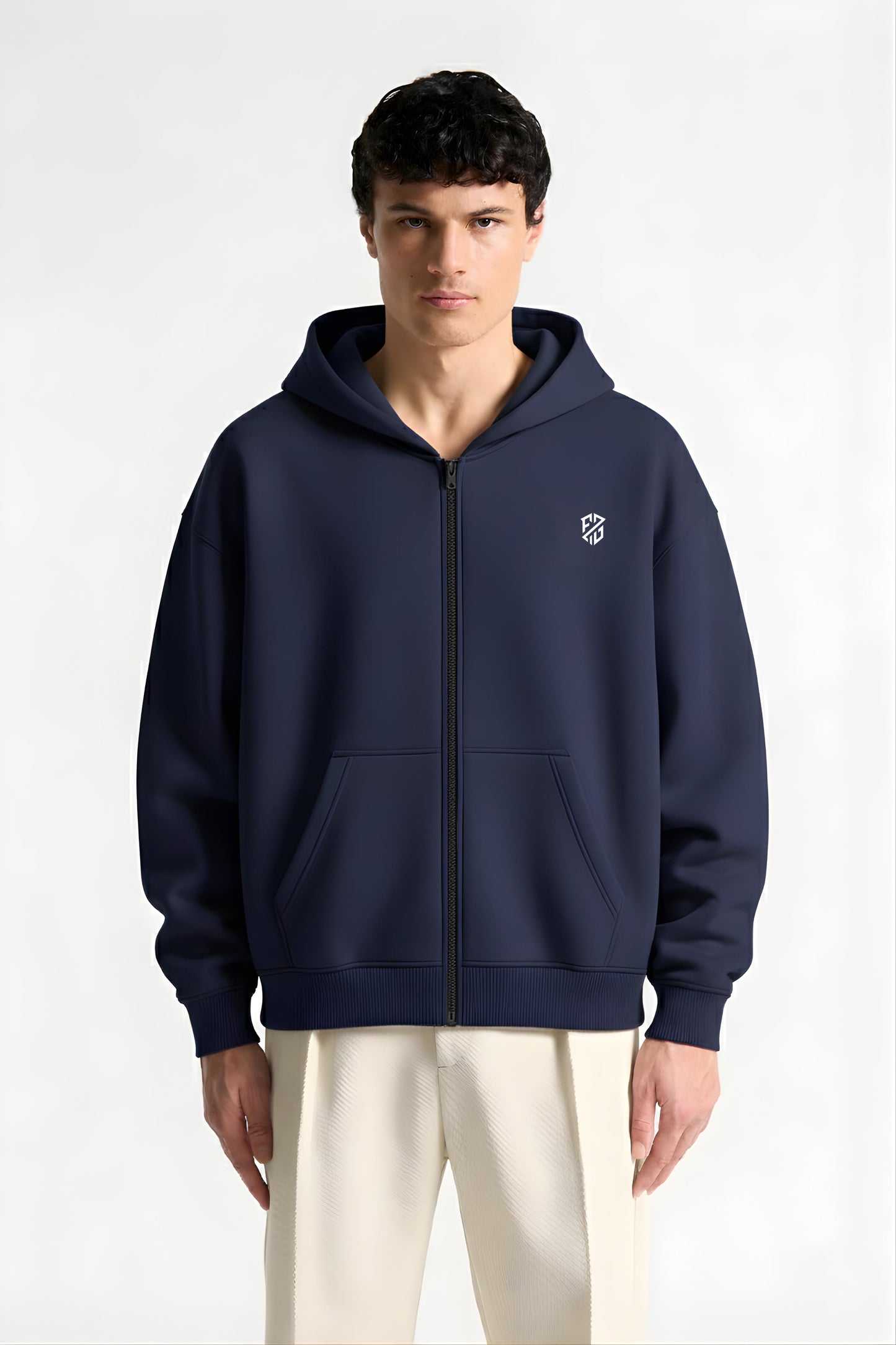 Man wearing navy blue zip-up hoodie with white logo and cream pants, front view