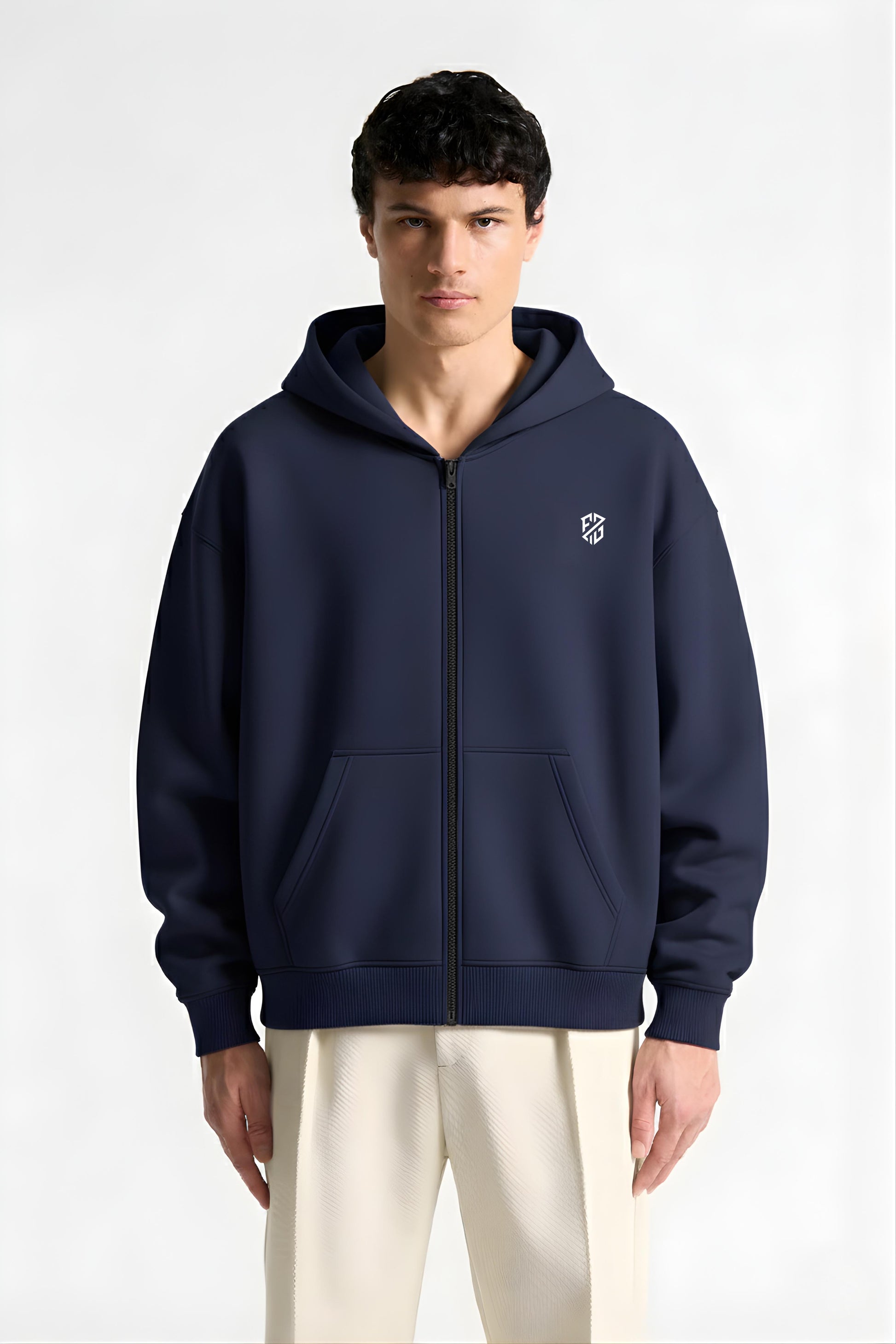 Man wearing navy blue zip-up hoodie with white logo and cream pants, front view