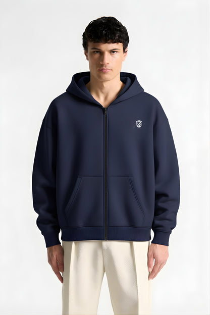 Man wearing navy blue zip-up hoodie with white logo and cream pants, front view