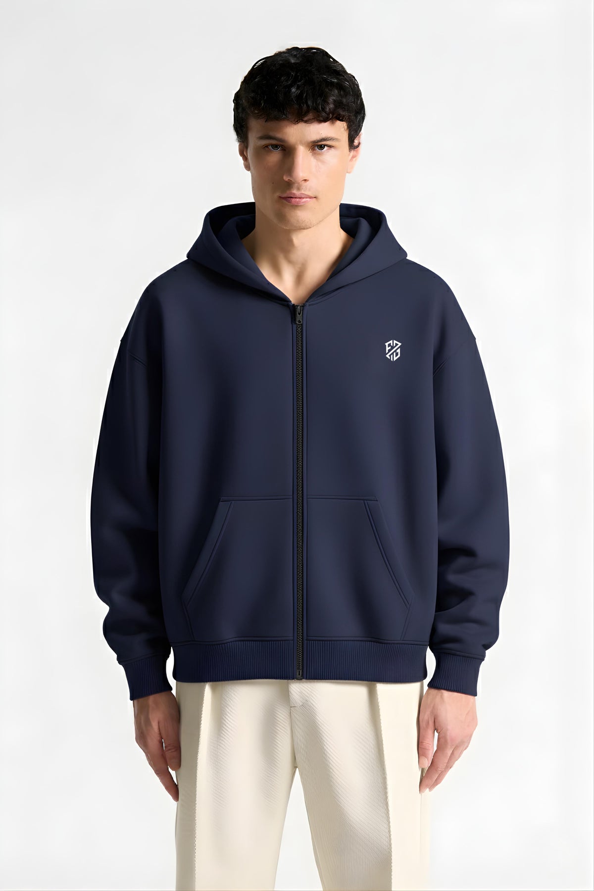 Man wearing navy blue zip-up hoodie with white logo and cream pants, front view
