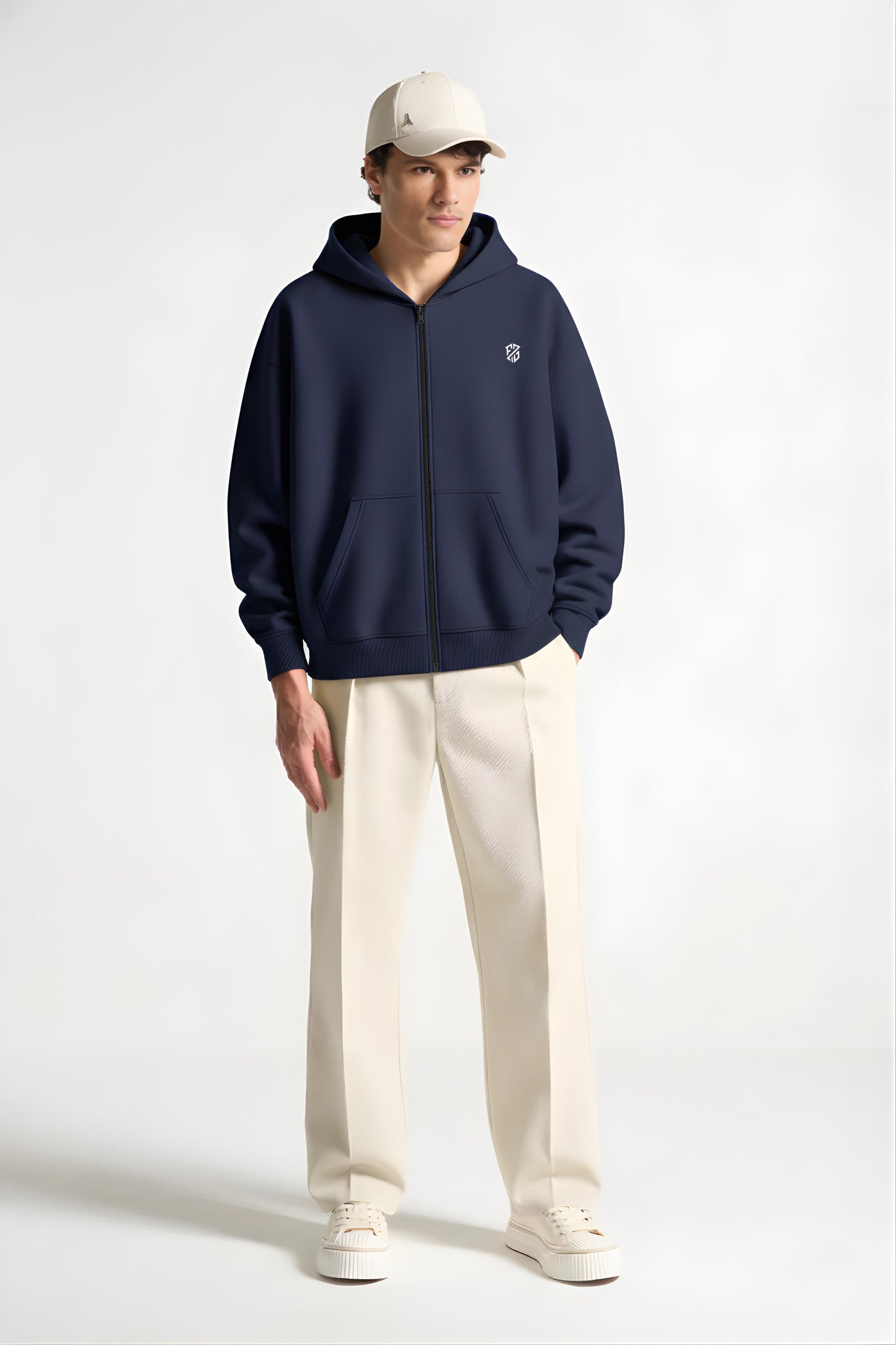 Man wearing navy zip-up hoodie, cream wide-leg pants, cream sneakers and cap, studio background