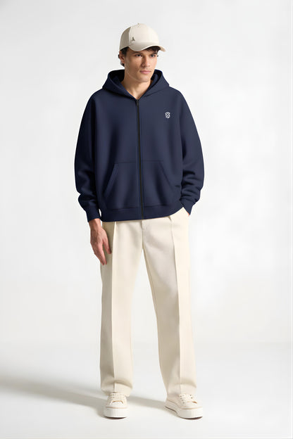 Man wearing navy zip-up hoodie, cream wide-leg pants, cream sneakers and cap, studio background