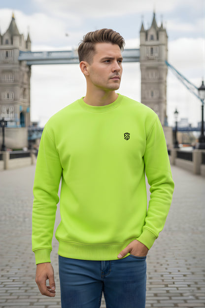 Man in neon green sweatshirt and blue jeans standing outdoors near a stone bridge
