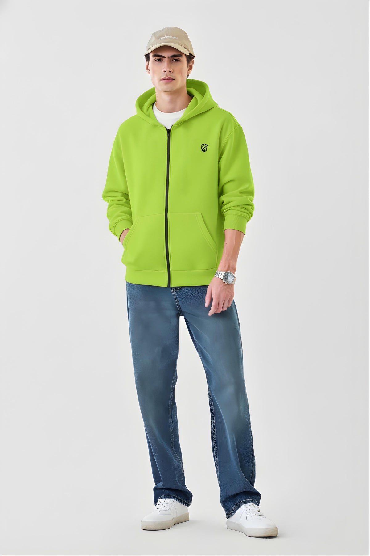 Man in light green zip-up hoodie, blue jeans, white sneakers, and beige cap on plain background