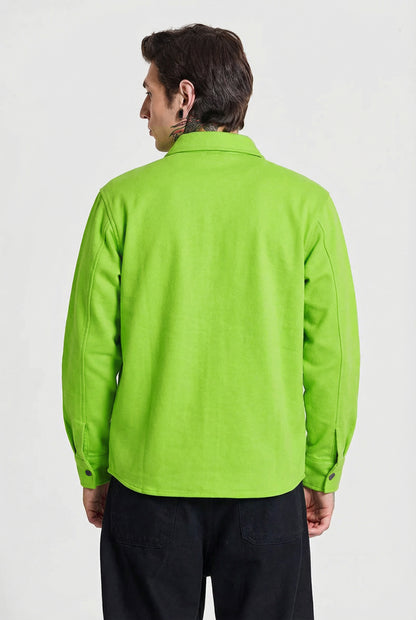 Man wearing bright green long sleeve shirt viewed from the back, black pants, studio background