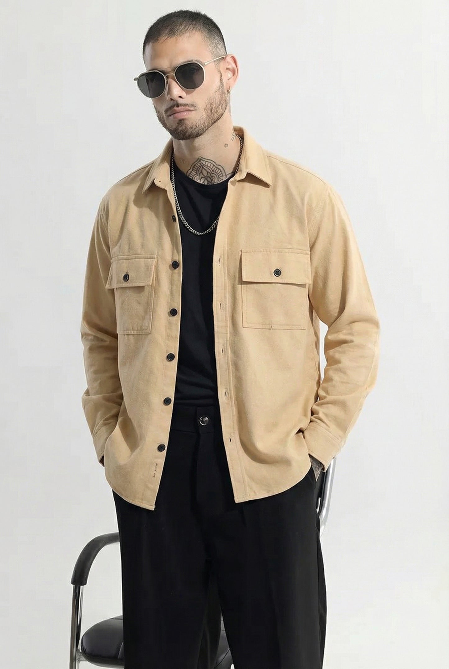 Man wearing beige button-up overshirt with front pockets, black pants, and sunglasses