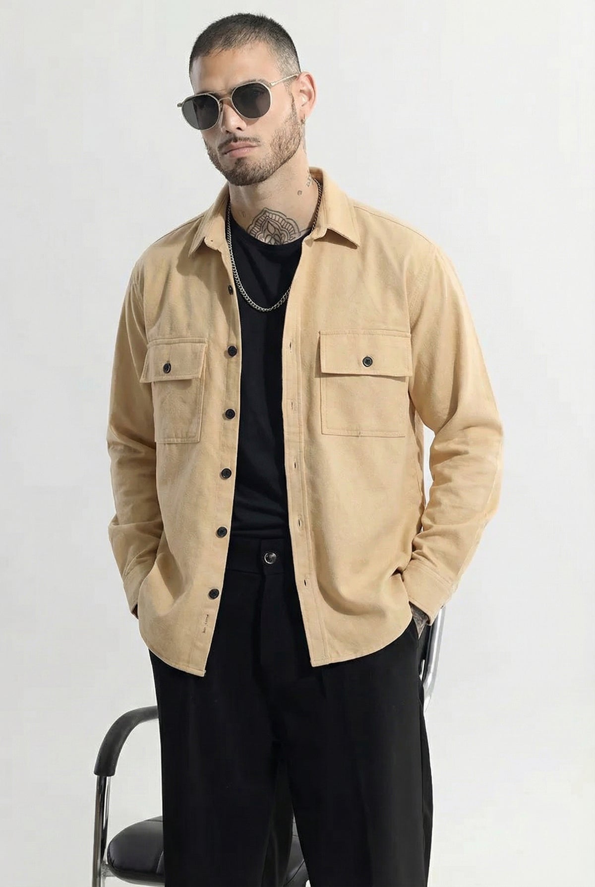 Man wearing beige button-up overshirt with front pockets, black pants, and sunglasses
