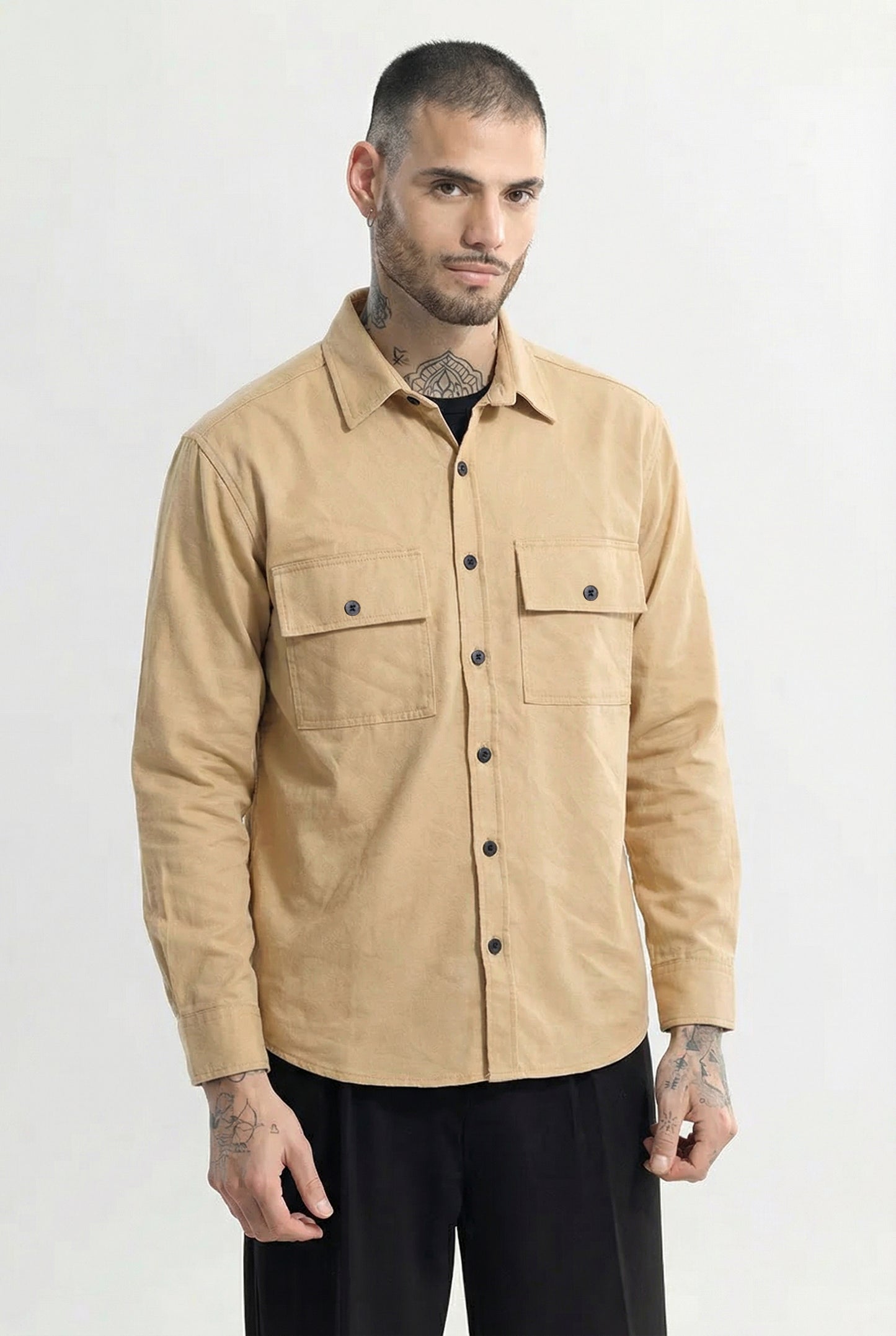 Man wearing beige button up shirt with chest pockets, casual fashion against plain background