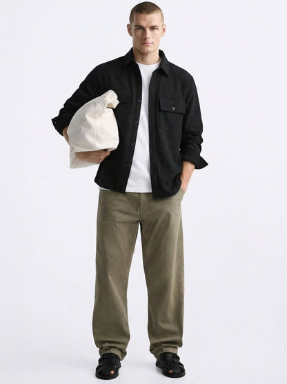Man in black overshirt, white t-shirt, olive pants, holding cream bag, black sandals