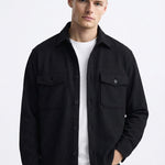 Man wearing a black button-up overshirt with chest pockets over a white t-shirt