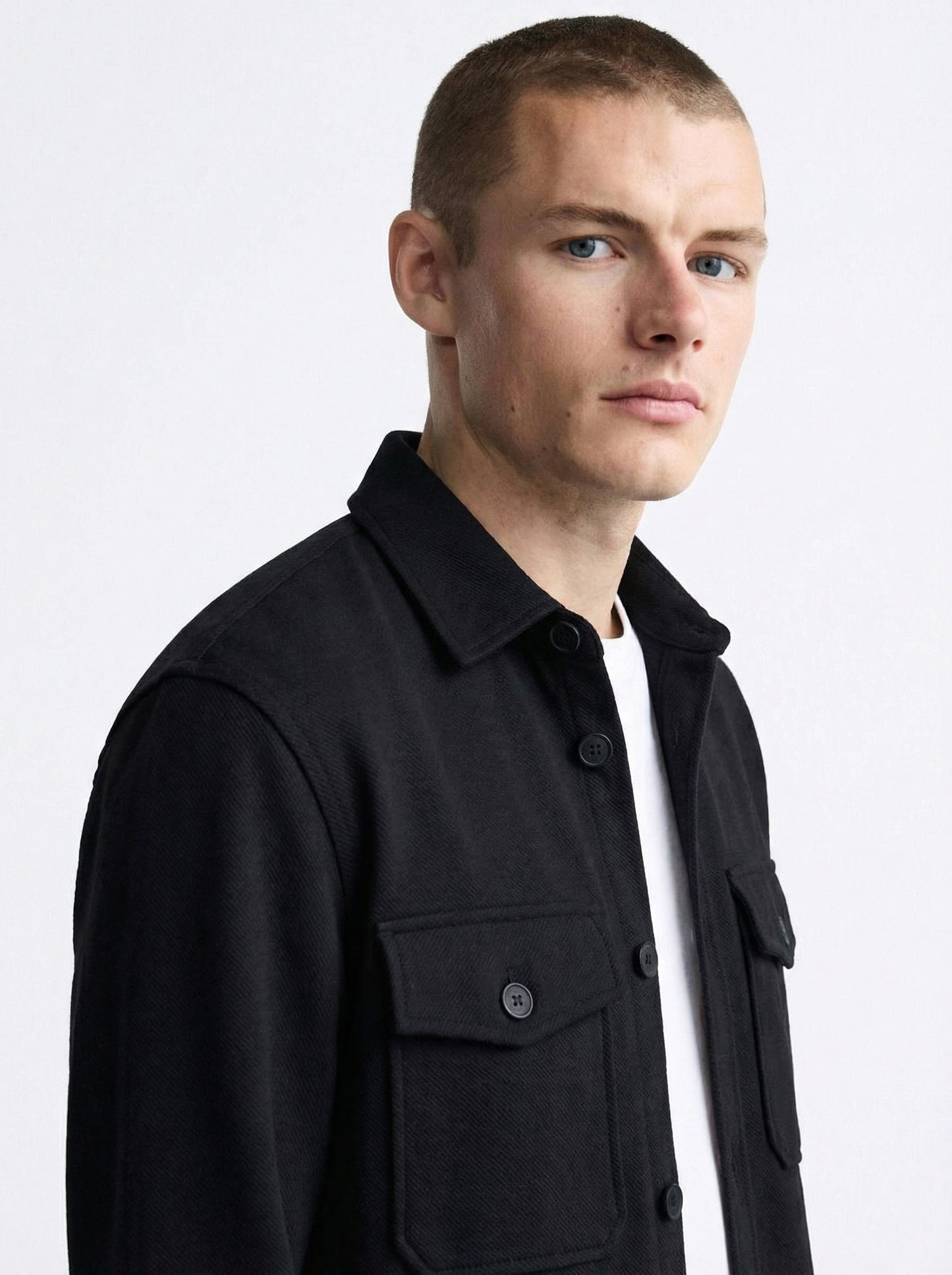 Man wearing a black button-up shirt jacket with flap chest pockets and a white t-shirt