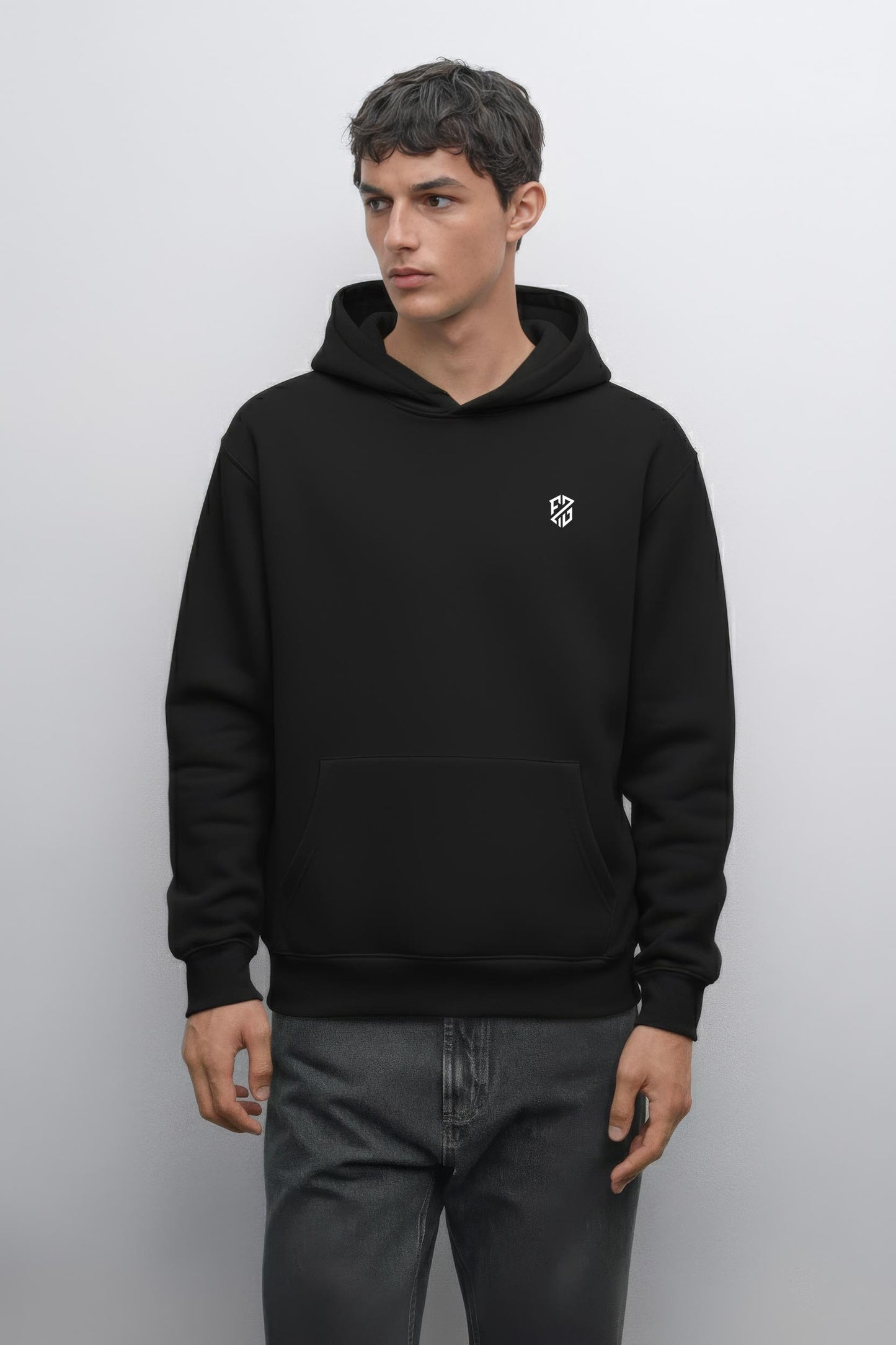 Man wearing a black hooded sweatshirt with a small white geometric logo on chest