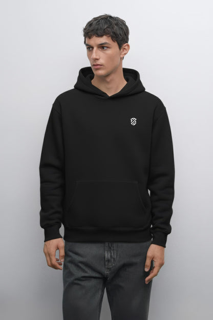 Man wearing a black hooded sweatshirt with a small white geometric logo on chest