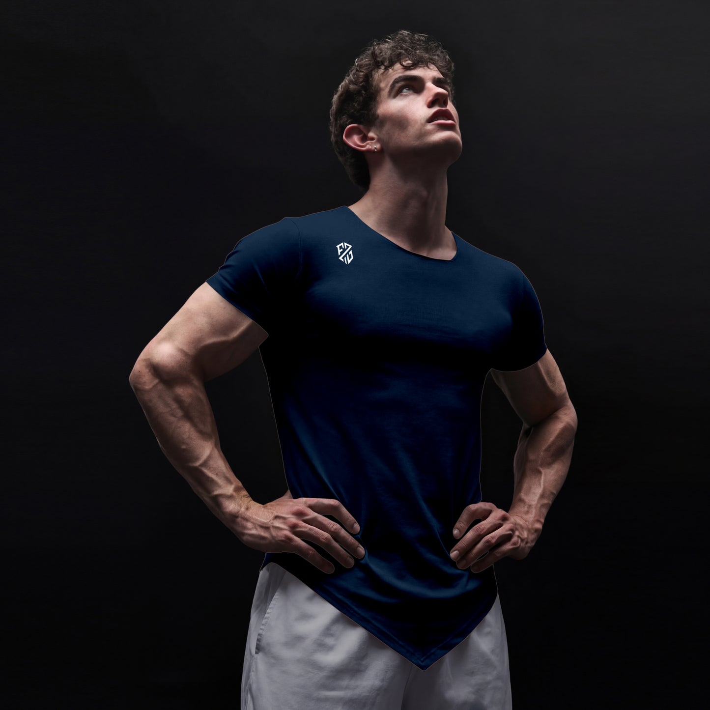 Athletic man in navy blue fitted t-shirt and white shorts posing confidently against black background