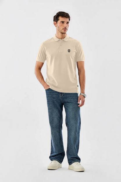 Man wearing beige polo shirt with black logo, blue jeans, white sneakers on white background