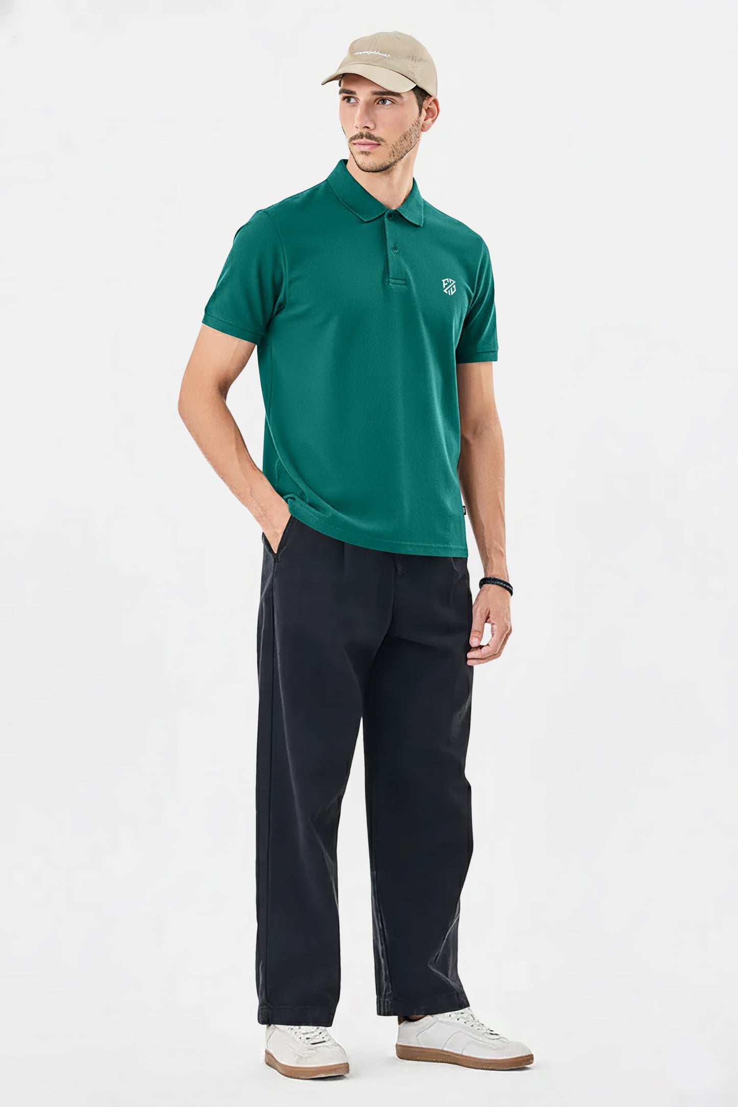 Man wearing green polo shirt, black pants, beige cap, and white sneakers on white background
