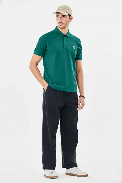 Man wearing green polo shirt, black pants, beige cap, and white sneakers on white background