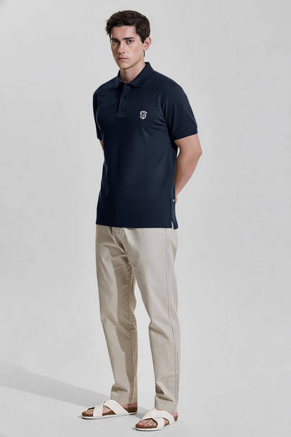 Man wearing navy polo shirt with chest logo, beige pants, and white sandals