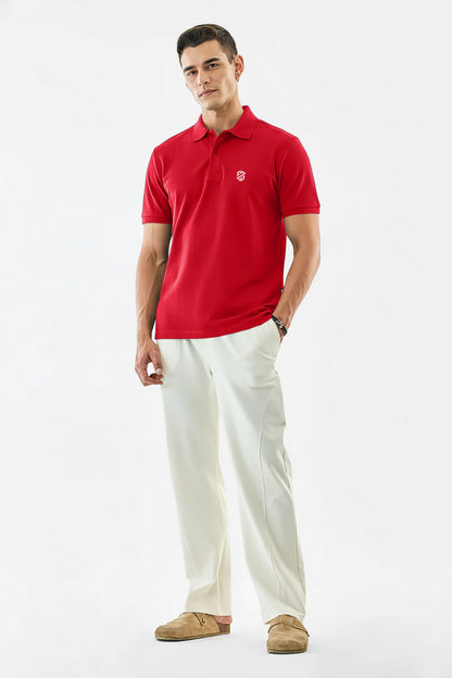 Man wearing a red polo shirt with logo, white trousers, and tan loafers on white background